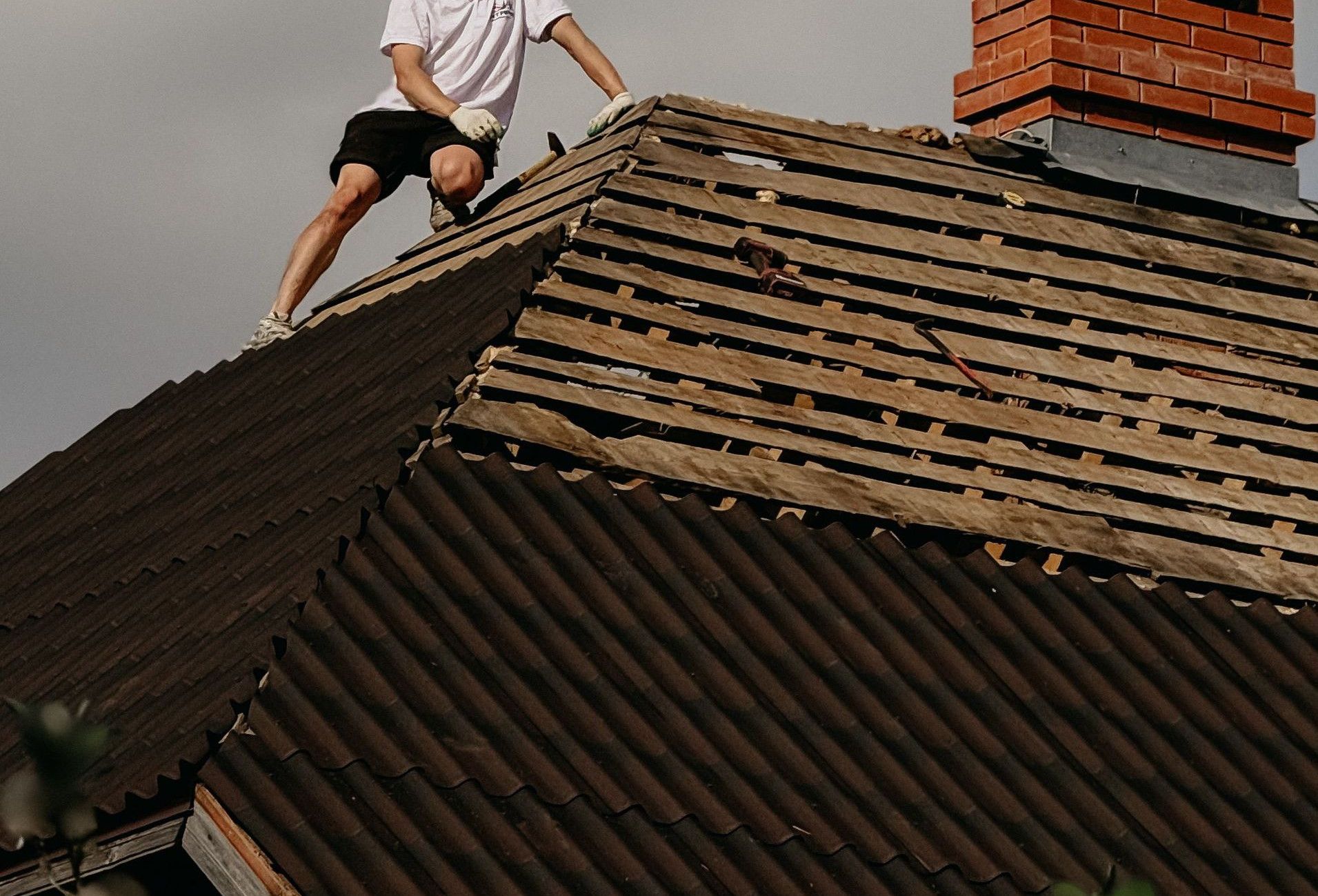Man in safety helmet repairing roof of red brick house under clear sky.